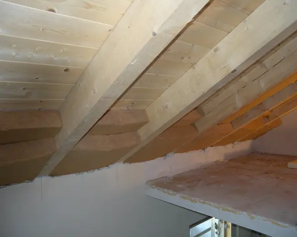 Isolamento tetto dall'interno fai da te: pannelli isolanti in fibra di legno tra le travi di legno grezzo, con sottotetto in perline.