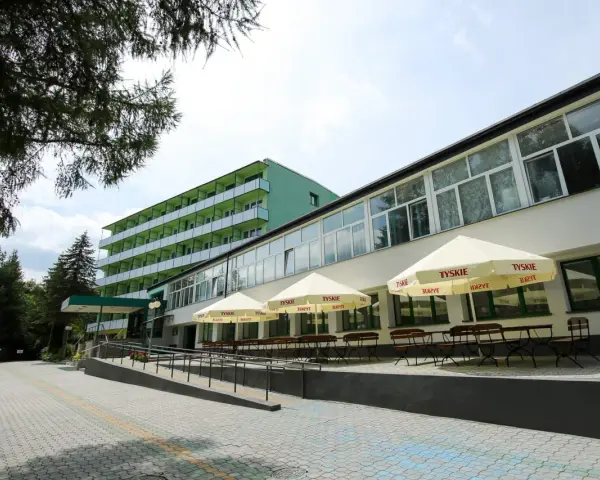 Tanie sanatorium prywatnie: zielony budynek z balkonami i tarasem z parasolami Tyskie.