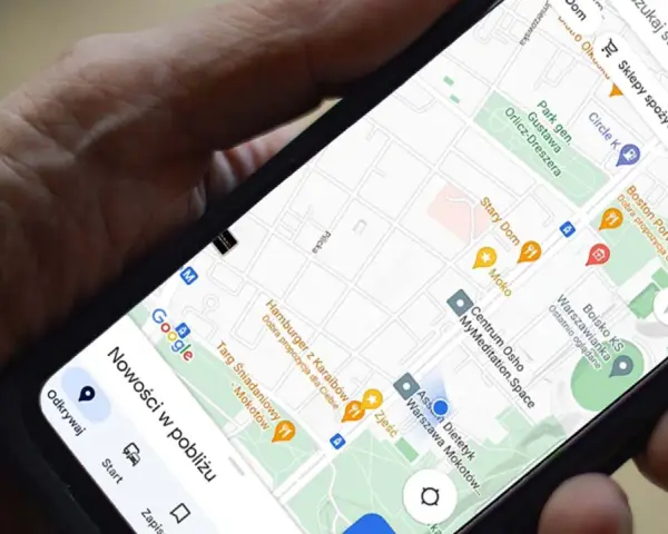 Dłoń trzyma telefon z mapą. Aplikacja do udostępniania lokalizacji pokazuje pobliskie restauracje i sklepy.