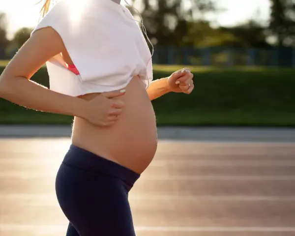 En gravid kvinna springer på en löparbana i solnedgången.