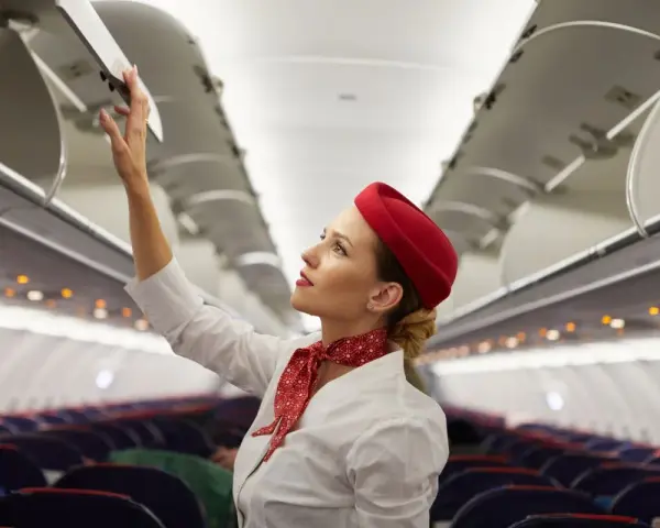 Flugbegleiterin schließt Gepäckfach. Ein Beruf, der mehr als nur das Flugbegleiter Gehalt bietet.