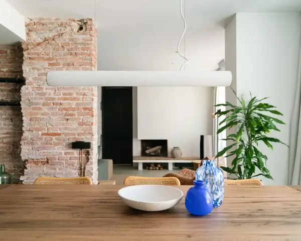 Salón con pared de ladrillo visto, mesa de madera con jarrones y planta.