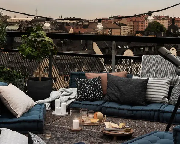 Gemütliche Lounge-Ecke auf einem grossen Balkon mit Blick über die Stadt. Kissen, Decken, Kerzen und ein Teleskop laden zum Entspannen ein.