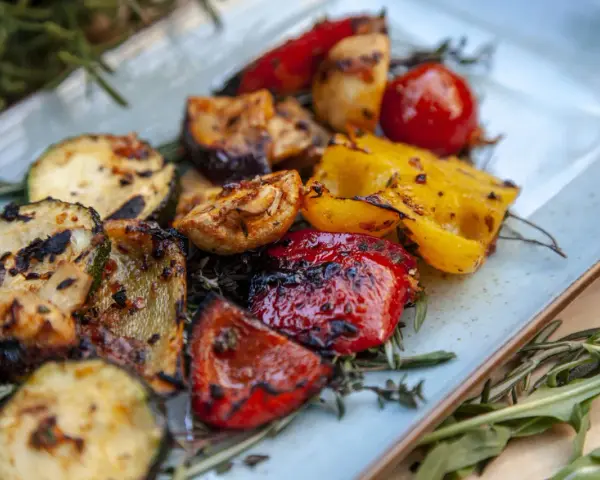 Gegrilltes Gemüse wie Zucchini, Paprika und Tomaten, garniert mit Rosmarin. Perfekt für Ihre nächsten BBQ Rezepte!
