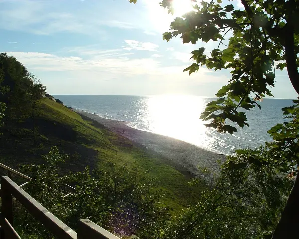 Słoneczny dzień nad morzem, łagodne zbocze porośnięte trawą schodzi do plaży. Jastrzębia Góra atrakcje to spacer po klifie i podziwianie widoków.