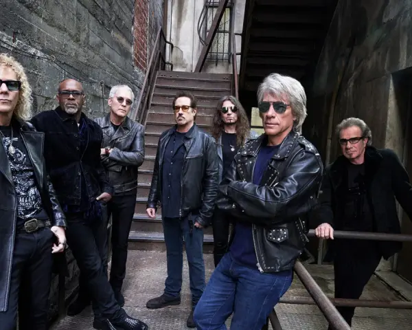 Zespół Bon Jovi gotowy na koncert, w skórzanych kurtkach i okularach przeciwsłonecznych, pozuje na tle industrialnych schodów.