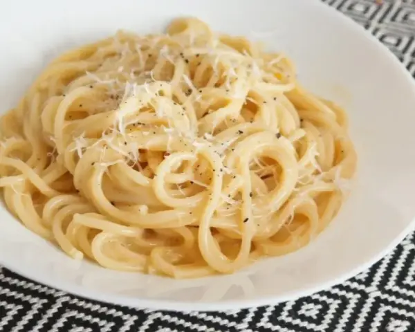 Pyszne spaghetti carbonara przepis na talerzu, posypane parmezanem i świeżo mielonym pieprzem.