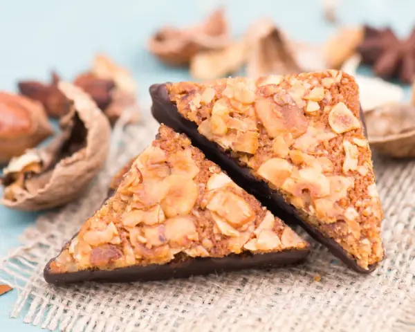 Zwei dreieckige Nussecken mit Schokoladenboden, bestreut mit gehackten Nüssen. Ein köstliches nussecken rezept zum Nachbacken.