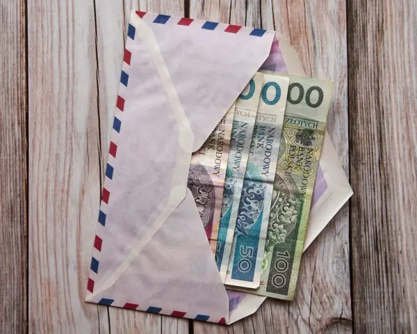 Koperta z pieniędzmi, zastanawiasz się, ile daje chrzestny na komunię? Widoczne banknoty 50 i 100 zł.
