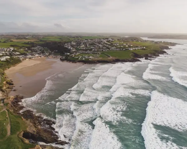 Aerial videography captures a coastal village with a sandy beach and rolling waves.