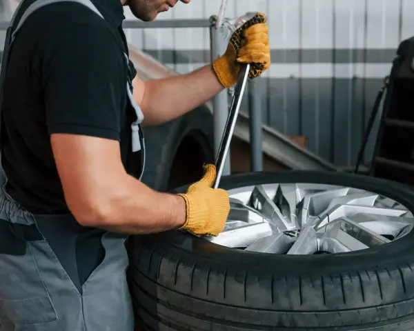 Mechanik w żółtych rękawicach używa klucza, by pokazać, jak zdjąć oponę z felgi.