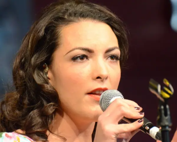 Caro Emerald śpiewa do mikrofonu, zbliżenie na twarz i dłonie.