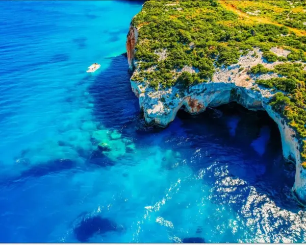 Błękitne morze i klify z jaskiniami to idealne miejsca na Zakynthos, co zobaczyć. Mała łódka kołysze się na falach.