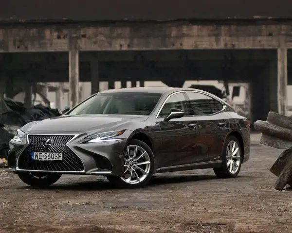 Szary Lexus LS 500h zaparkowany na tle zniszczonej budowli.