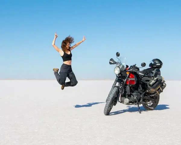 Donna salta di gioia su un deserto di sale, moto pronta per l'avventura. Questo è cosa significa on the road: libertà e scoperta.