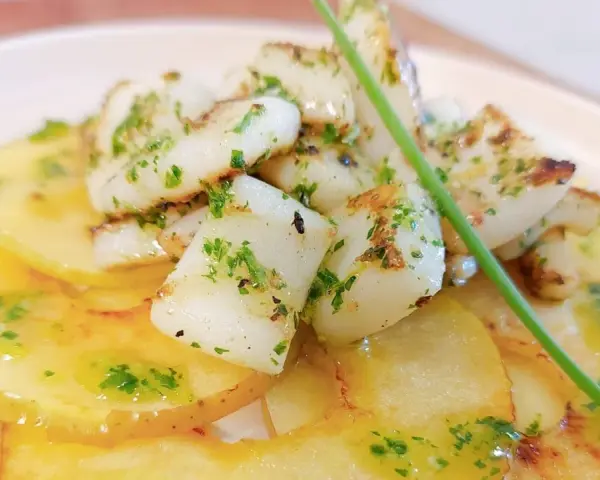 Delicioso plato de sepia al ajillo sobre patatas finas, con perejil picado y un toque de aceite de oliva.