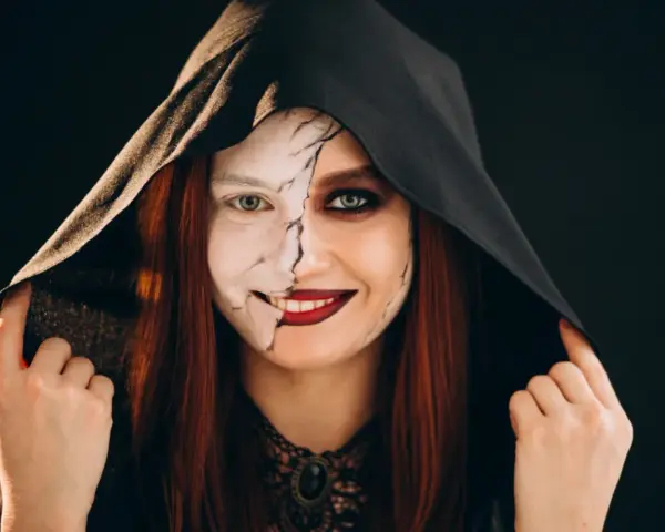 Kobieta w kapturze z połową twarzy pomalowaną na biało, z pęknięciami, druga połowa z ciemnym makijażem. Idealny prosty makijaż na Halloween.