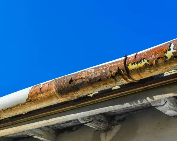 Gouttière en zinc très rouillée, nécessitant une réparation urgente. Le ciel bleu contraste avec la dégradation du matériau.