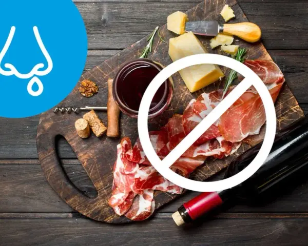 Deska serów i wędlin z winem, z symbolem zakazu. Wskazuje na dietę antyhistaminową, unikającą pewnych produktów.