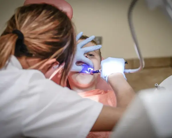 Dentysta w rękawiczkach bada zęby dziecka przy użyciu niebieskiego światła.
