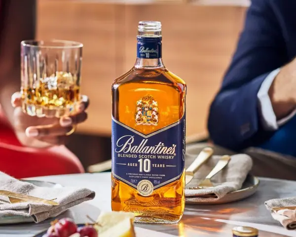 Elegancka butelka Ballantine's 10 Years Old na stole, obok kieliszka z bursztynowym płynem. To nie bourbon, lecz szkocka whisky, idealna na specjalne okazje.