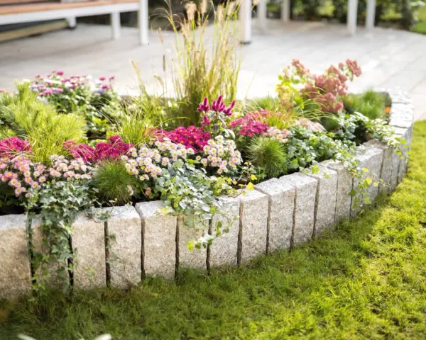 Ein wunderschön bepflanztes Beet mit bunten Blumen und Gräsern, umrandet von Granitsteinen. Perfekt, um neue Ideen für eigene Beet planen zu sammeln.