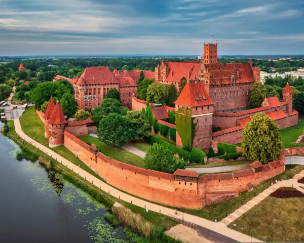 Malbork, największy zamek w Polsce, majestatycznie wznosi się nad rzeką Nogat. Czerwona cegła i strzeliste wieże tworzą imponujący widok.