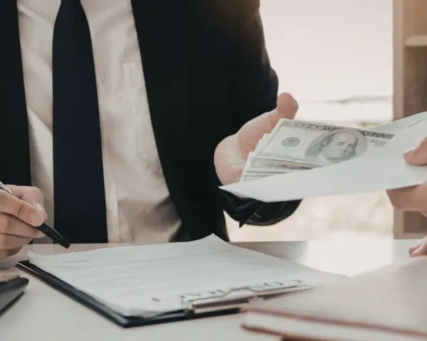 Biznesmen przekazuje kopertę z pieniędzmi, podczas gdy drugi mężczyzna podpisuje dokument. Szybka gotówka windykacja terenowa.