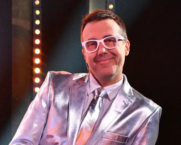 DJ Adamus w srebrnym garniturze i białych okularach, uśmiecha się. Czy to jego odpowiedź na pytanie "Jaka to melodia?