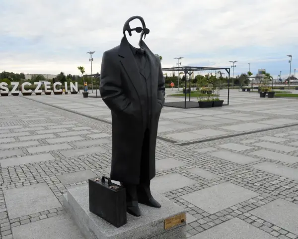 Pomnik Krzysztofa Jarzyny w Szczecinie, z charakterystyczną teczką u stóp, stoi na placu z napisem "SZCZECIN" w tle.