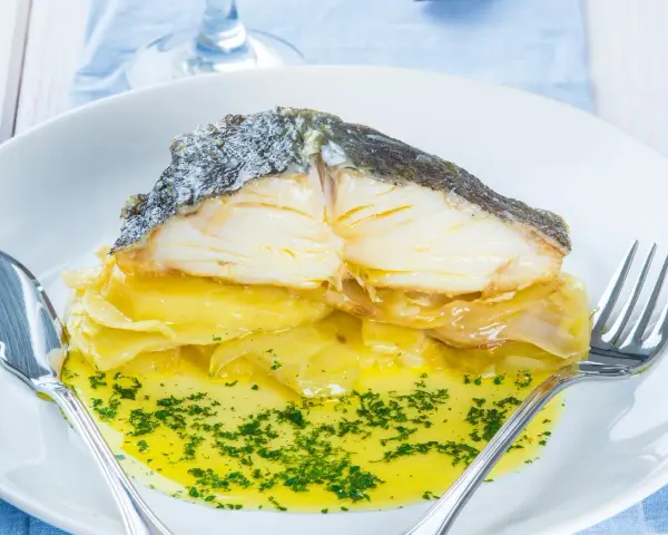 Pescado al horno con patatas y cebolla, bañado en aceite de oliva y perejil. Un plato delicioso y reconfortante.