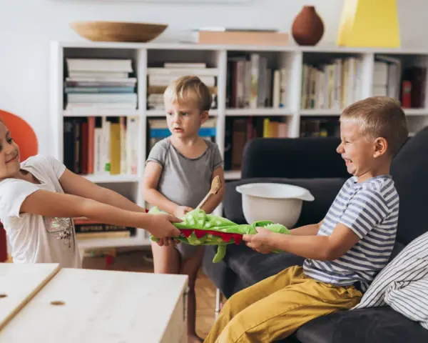 Zwei Kinder im **Streit mit Schwester** um ein Stofftier. Ein kleiner Junge schaut zu.