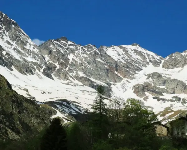 Imponente montagna sacra innevata, con un piccolo campanile bianco che emerge tra gli alberi verdi in primo piano.