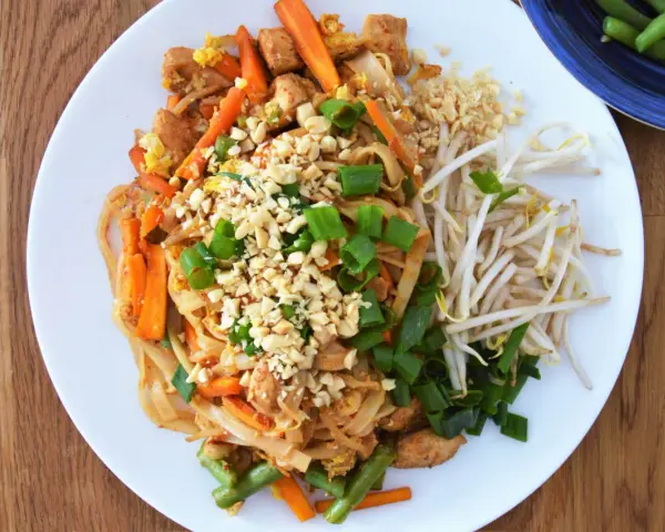 Pad Thai z kurczakiem, warzywami i orzeszkami ziemnymi na białym talerzu.