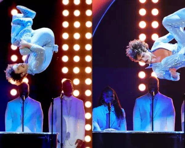 Wokalista w błyszczącym niebieskim stroju wykonuje akrobacje na scenie podczas gali nagród Grammy. Laureaci nagród grammy w białych garniturach stoją za fortepianami.