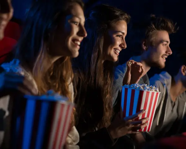Uśmiechnięci ludzie jedzą popcorn w kinie. Idealny strój do kina to coś wygodnego, jak na przykład bluza.