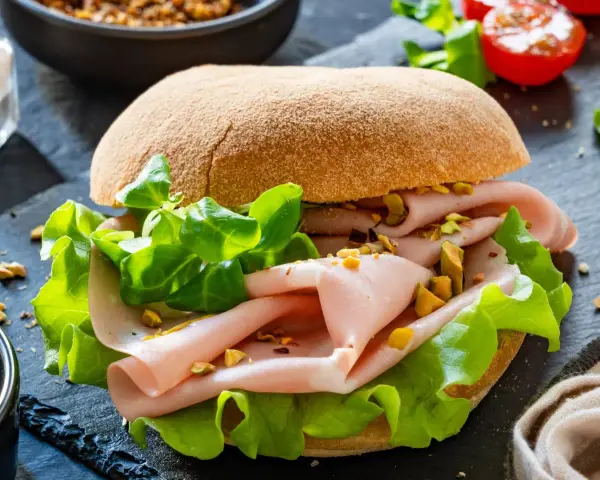 Pyszna włoska kanapka z mortadelą, chrupiącą sałatą i pistacjami na ciemnym tle.