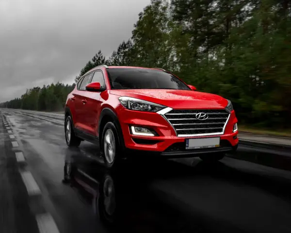 Czerwony Hyundai Tucson jedzie po mokrej drodze w deszczowy dzień. Warto pamiętać o filtrze CPL, którego zastosowanie poprawia widoczność w takich warunkach.