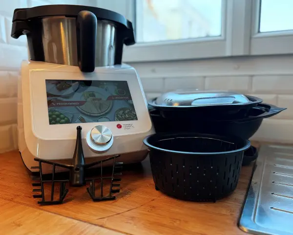 Robot culinaire Monsieur Cuisine Smart prêt à préparer une recette. Accessoires et bols empilés à côté.