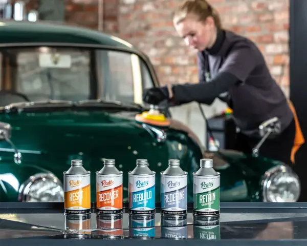 En kvinna polerar en grön bil med en maskin. Framför bilen står fem flaskor med bilvårdsprodukter, redo att vaxa bilen.