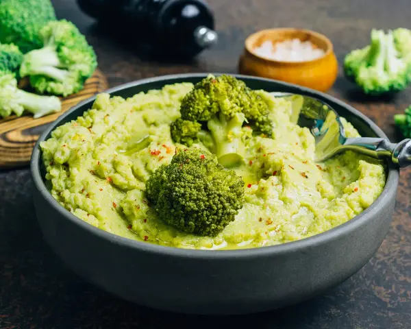Un bol de purée de brocolis onctueuse, garni de fleurettes de brocolis et d'épices rouges. Un délice vert et sain.