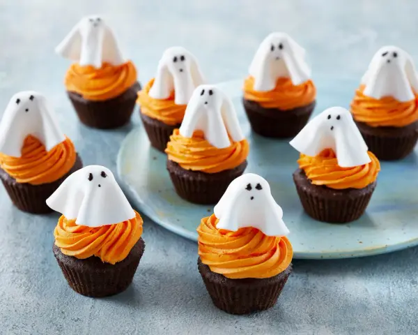 Sju chokladmuffins med orange frosting och vita spökdekorationer. Perfekt att baka till Halloween med barnen!