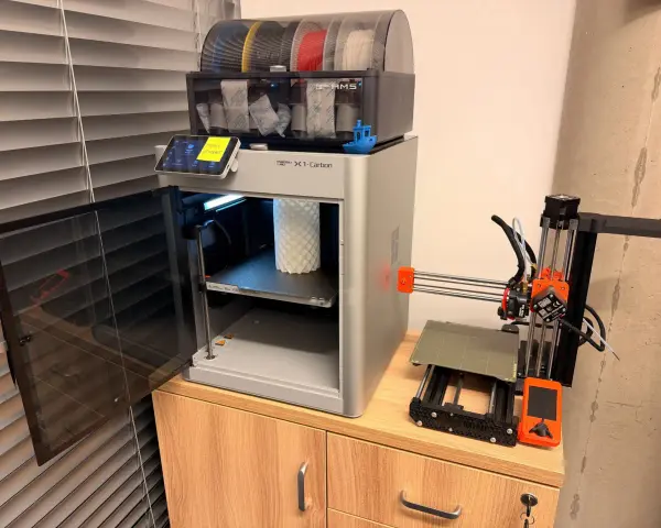 Test drukarki 3D Bambu Lab X1-Carbon z AMS i małą drukarką Prusa Mini obok.