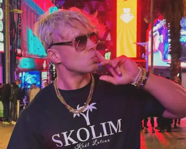 Skolim w okularach i złotych łańcuchach, pozuje na tle neonów. Król Latino w swoim wieku, w blasku miasta.