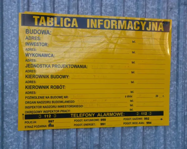 Tablica informacyjna budowy, gdzie można znaleźć dane o pozwoleniach na budowę domu, wykonawcach i numerach alarmowych.