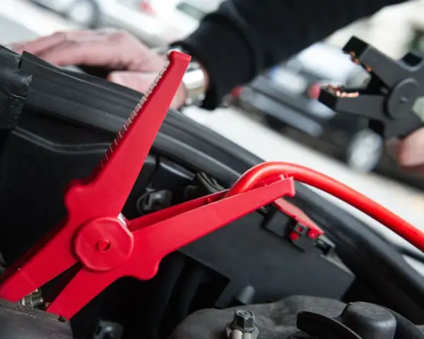 Rotes Kabel mit Krokodilklemme wird an Autobatterie angeschlossen. Plus oder Minus?