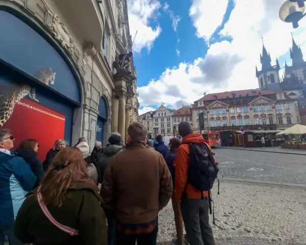 A group of tourists on a prague free walking tour gather on a cobblestone street, with historic buildings and a church in the background.