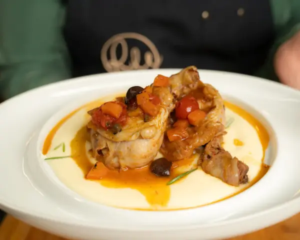 Pollo alla cacciatora succulento su un letto di polenta cremosa, guarnito con pomodorini, olive e carote.