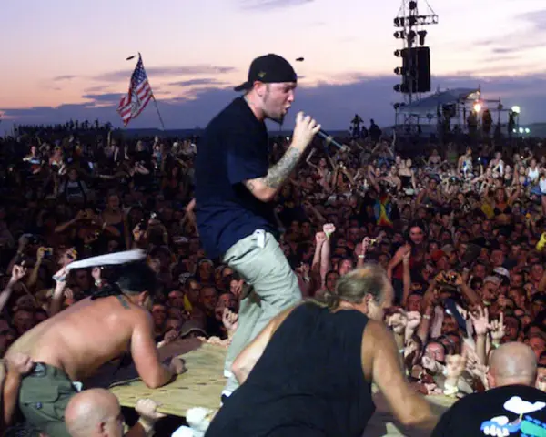 Tłum na Woodstock 99, z wokalistą na scenie i amerykańską flagą. Atmosfera była napięta, co doprowadziło do późniejszych zamieszek i ofiar.