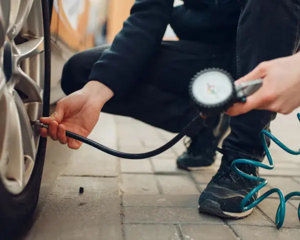 Persona controlla la pressione degli pneumatici dell'auto con un manometro, seguendo la tabella pressione pneumatici auto per la sicurezza.